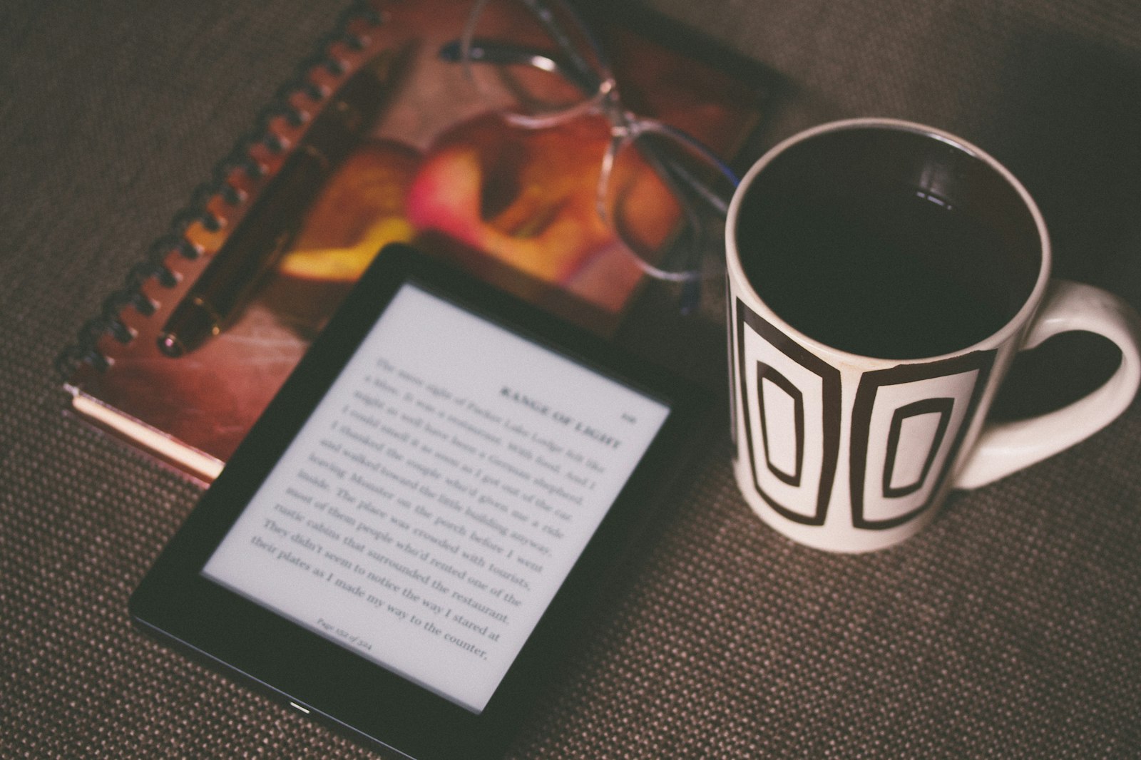 Электронная книга с E Ink-экраном рядом с блокнотом, ручкой и кружкой на столе