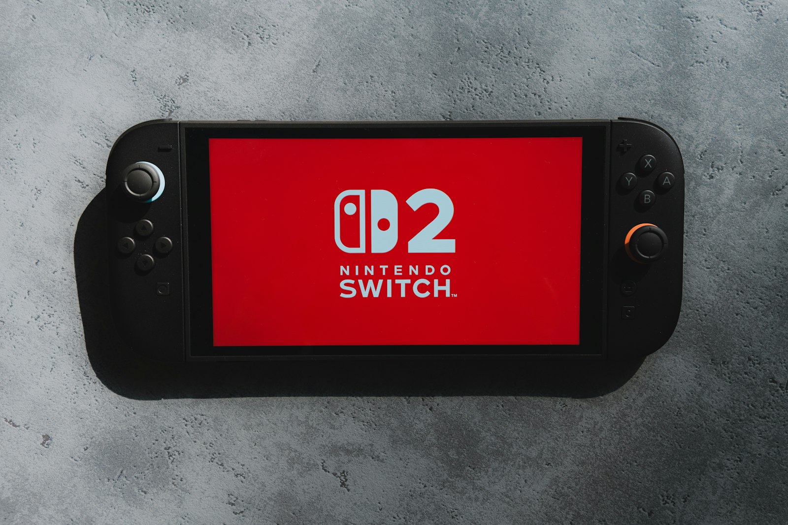 Nintendo Switch 2 — портативная игровая консоль с логотипом NS2 на экране, вид спереди на сером фоне