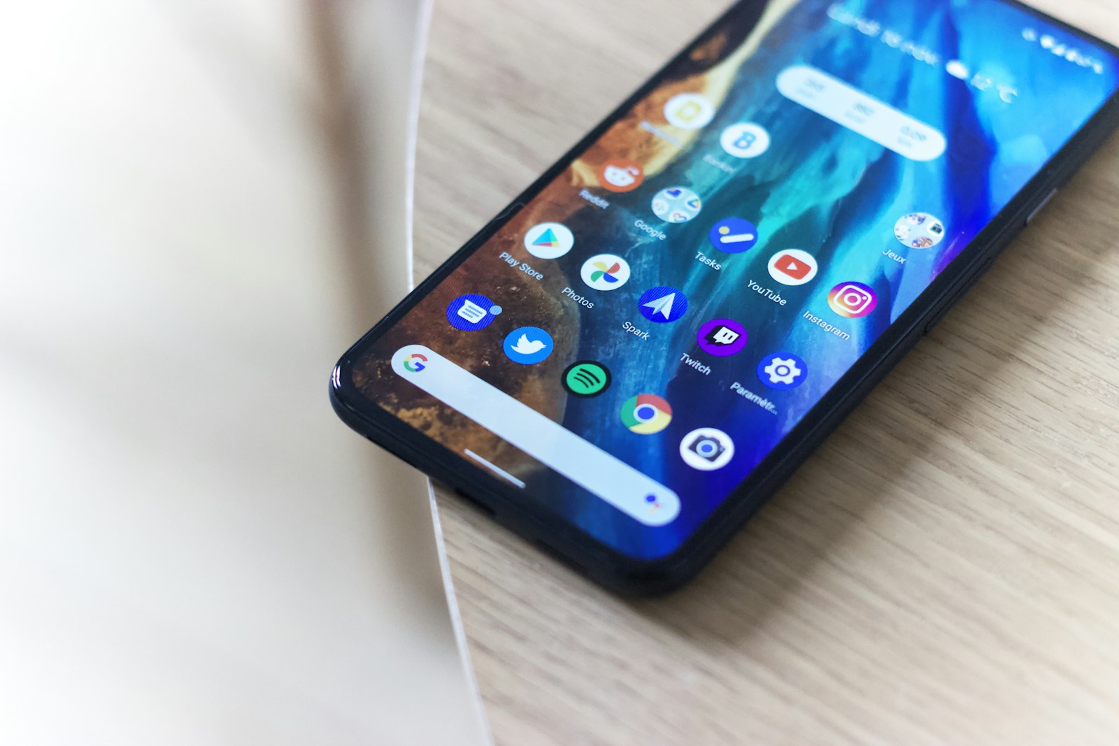 Современный Android-смартфон с большим экраном и сеткой приложений лежит на деревянном столе