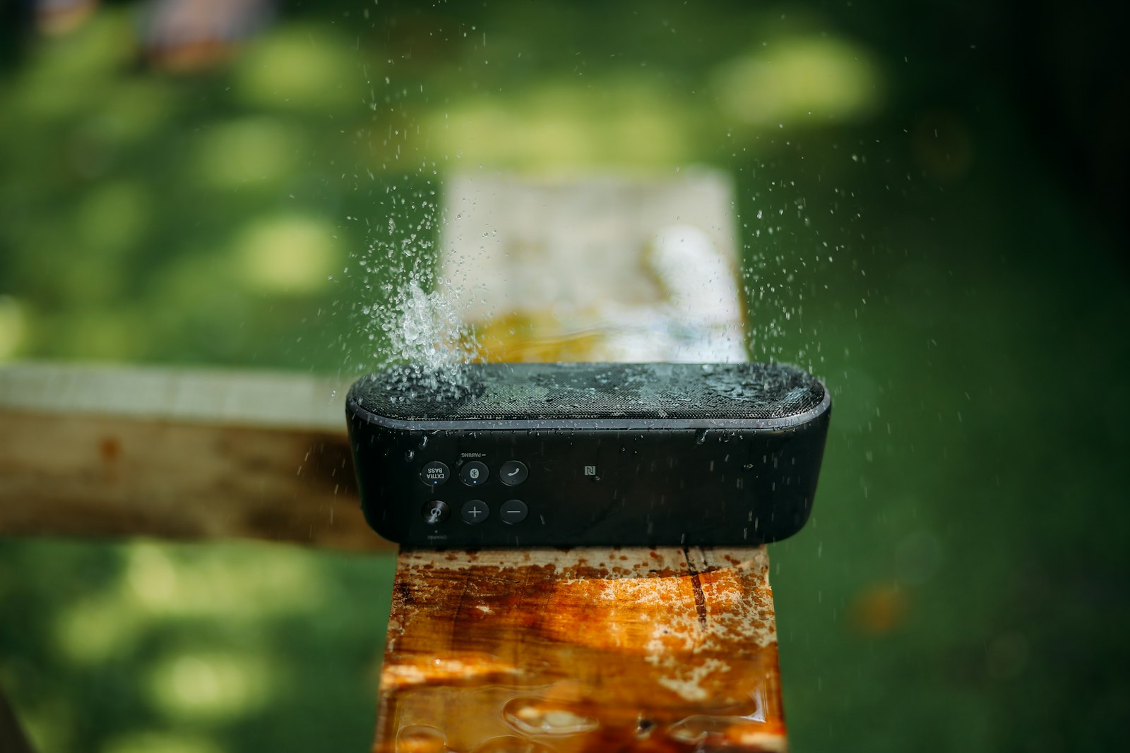 Портативная влагозащищённая Bluetooth-колонка под брызгами воды на деревянной опоре