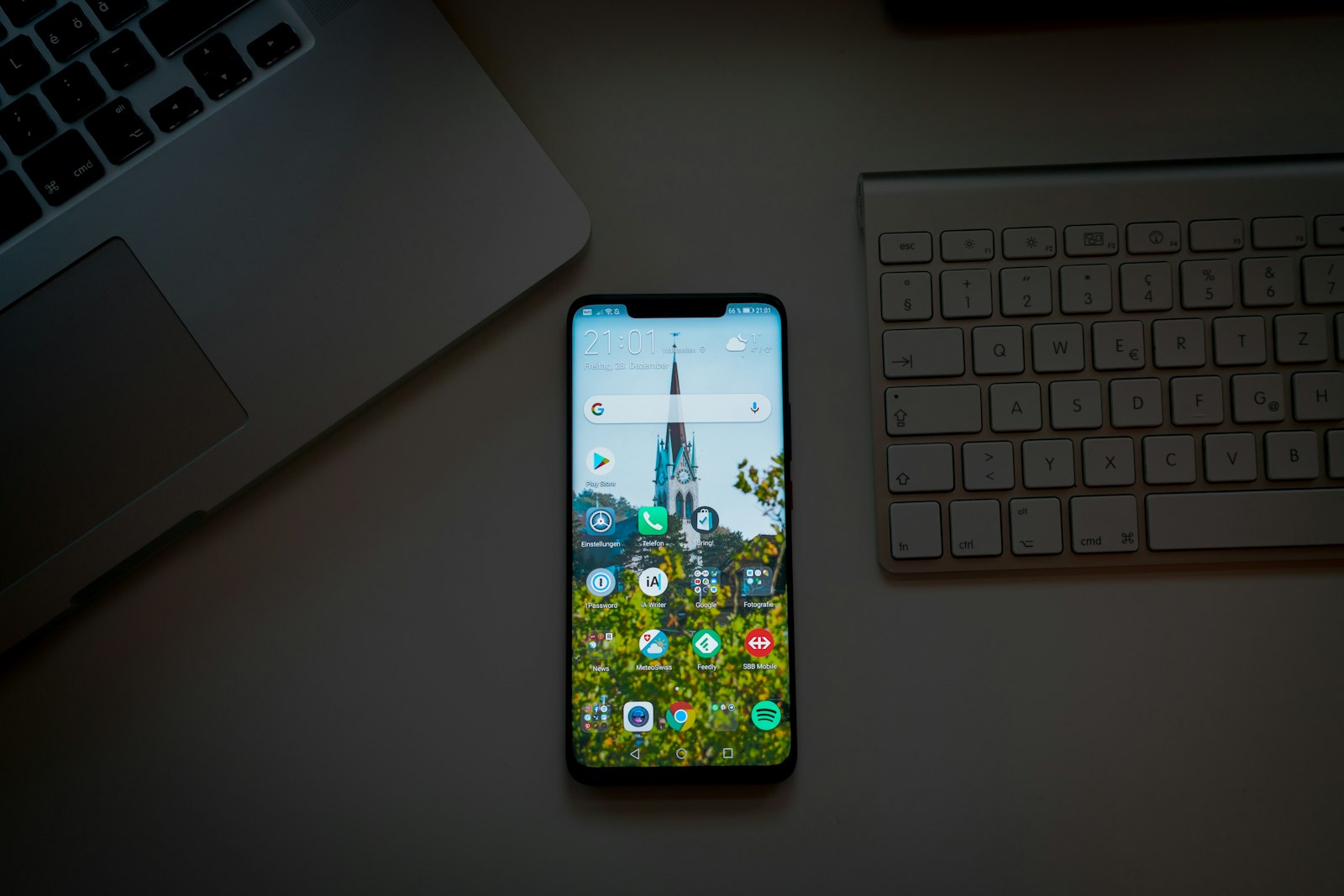 Android-смартфон с безрамочным экраном лежит на рабочем столе рядом с ноутбуком и клавиатурой